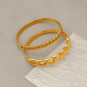 Close-up of gold titanium steel bangle and Cuban chain link bracelet set on texture