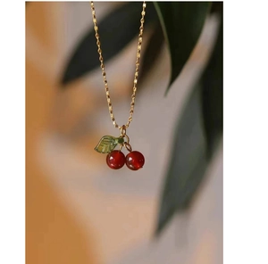 Close-up of a gold cherry pendant necklace with red beads and a green leaf charm