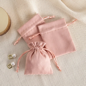 Pink velvet jewelry pouch with drawstring and flap closure on beige grid fabric background