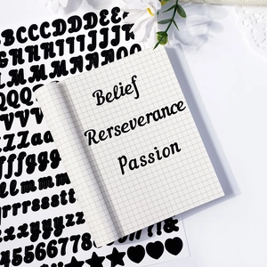 Close-up of black textured vinyl letter stickers on a white grid journal with floral decor