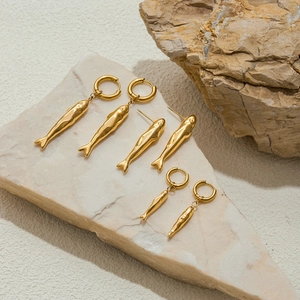 Detailed view of hammered 18k gold fish earrings on natural stone for a modern aesthetic