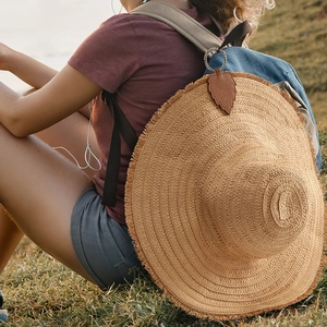 Leaf shaped brown PU leather magnetic hat clip attached to a straw hat on a backpack