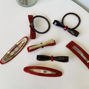 Close-up of elegant red and black bow hair ties and golden hair clips on white surface
