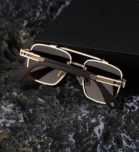 Detail of square gold metal sunglasses featuring engraved temples and dark gray lenses