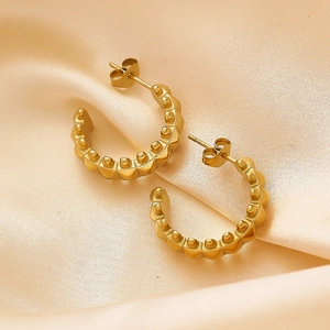 Close-up of golden C-shaped stud earrings with studded texture on pink satin fabric