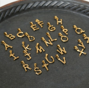 Macro shot of gold-plated 18K titanium steel bamboo style alphabet letter charms in a tray