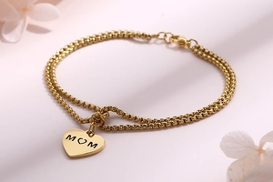 Detailed shot of double-layered gold bracelet with heart MOM pendant on pink background