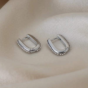 Macro di orecchini a U in argento con zirconi su un elegante fondo in seta beige