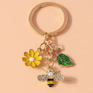 Detail of bee keychain with yellow daisy, green leaf, and pearl accents on gold ring