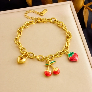 Close-up of gold chain bracelet with red cherry, strawberry and heart lock charms