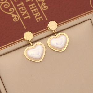 Detail of gold heart pendant earrings with pearl inlay resting on a jewelry box