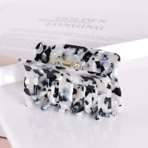 Detail of square acetate hair claw with black and white marble pattern and gold spring