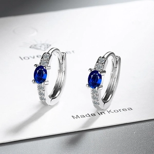 Close-up of silver hoop earrings featuring oval blue gemstones and white zircon accents