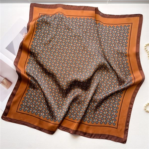 Detailed view of square silk scarf with geometric patterns and caramel tones on white desk