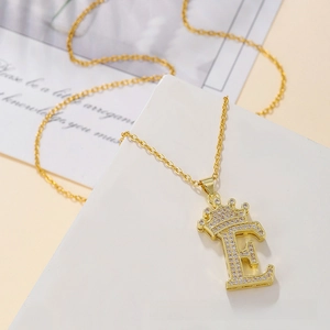 Macro detail of gold crown letter E pendant with cubic zirconia and dainty chain