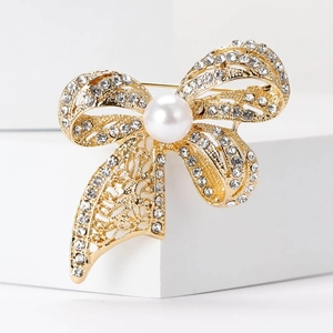 Elegant gold bow brooch with sparkling rhinestones and a large pearl on white stand