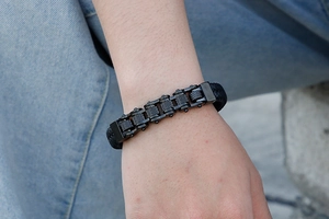 Close-up of black braided leather bracelet with industrial metal gear chain on wrist