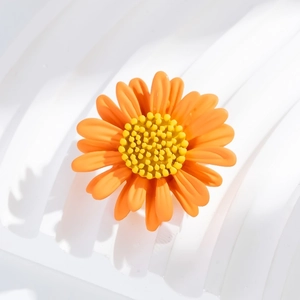 Macro shot of 3D orange daisy flower brooch with textured yellow center on white pedestal