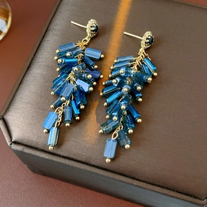 Detail of blue beaded gold fringe earrings with inlaid dark gemstone and tassel