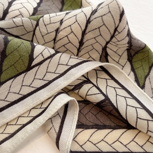 Close-up of beige fashion silk scarf with green leaf patterns and woven texture details