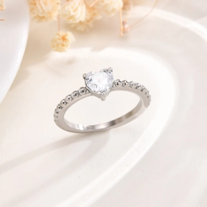 Dettaglio dell'anello con zircone a cuore e fascia a sfere su superficie di lusso