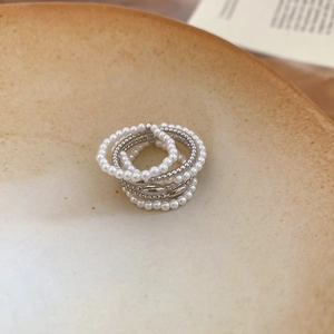 Detail view of multi-layer pearl rings and metallic bands on a ceramic tray