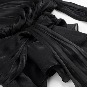 Detail of the black dress featuring a stylish knot design and pleated fabric texture