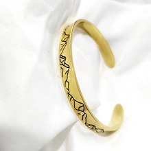 Close-up of golden stainless steel cuff bracelet with engraved mountain pattern texture