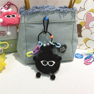 Détail d'un porte-clés monstre en peluche noire avec lunettes sur un sac en jean bleu