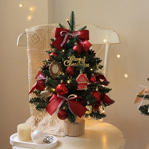 Mini decorated Christmas tree with LED lights and golden Merry Christmas sign on wood chair