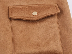 Détail d'un blouson aviateur en daim marron montrant une poche plaquée et bouton doré