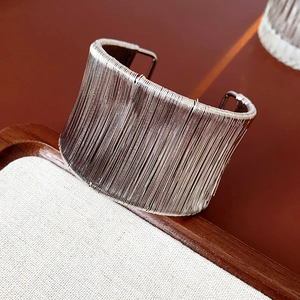 Dettaglio del bracciale rigido argento largo con texture a fili paralleli su legno