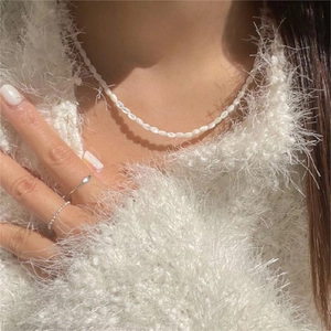 Detail of elegant white rice pearl necklace and silver rings worn on a soft sweater