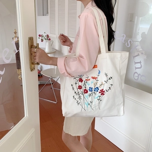 Detailed embroidery of colorful flowers on a white canvas tote bag with a small orange label