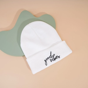 Close-up of white knitted beanie with black 'good vibes' embroidery and ribbed texture