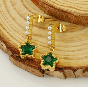 Détail de boucles d'oreilles étoile dorées avec gemmes vertes et perles sur bois