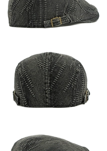 Detail of washed denim flat cap showing white contrast stitching and metal side buckle