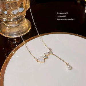 Close-up of golden necklace with heart pendants and a pearl on a white ceramic plate
