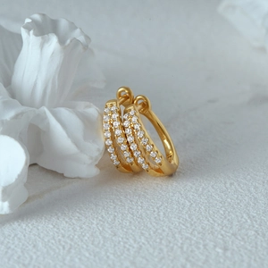 Detailed close-up of gold huggie earrings with triple row pave-set crystals on white floral
