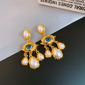 Detail of surrealist gold evil eye earrings with hanging white teardrop pearls
