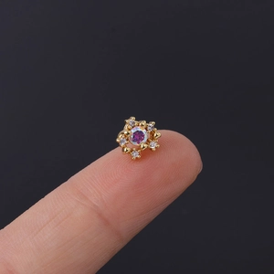 Macro shot of tiny gold cartilage stud with iridescent stone and white crystals on fingertip