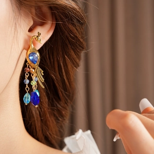 Close-up of vintage golden peacock earrings with blue gemstone and colorful beads on model