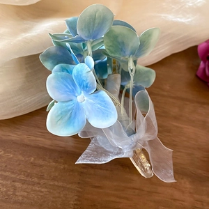Detail von blau-grünem Organza-Blumen-Haarclip mit transparenter Schleife auf Holzoberfläche