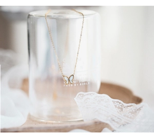 Detail of butterfly necklace with white shell inlay hanging on a glass over lace