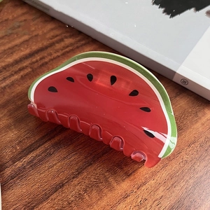 Detailed close-up of a watermelon-shaped hair claw clip with a glossy finish on wood