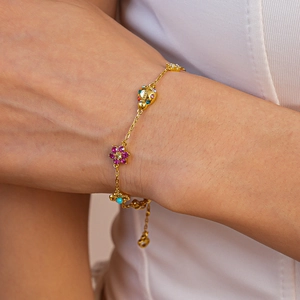 Close-up of a gold necklace featuring colorful zircon ladybug and flower charms on a model