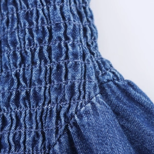 Detailed close-up of smocking texture and stitching on blue denim fabric dress