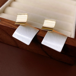Detailed close-up of geometric two-tone metal earrings on a wooden jewelry display box