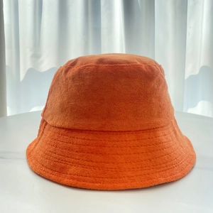 Detailed texture of orange terry cloth bucket hat on a clean white marble background