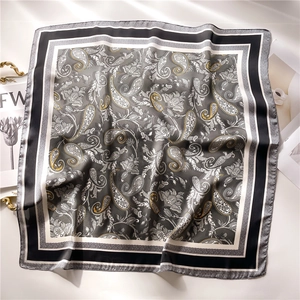 Detail of grey paisley silk scarf with glossy texture on a minimalist white table